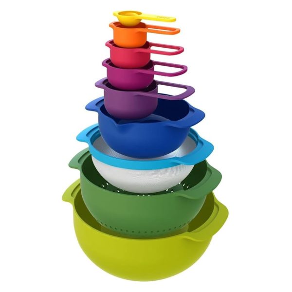 The Joseph Joseph Nest 9 set of colour-coded nesting bowls, measuring cups, a colander and a sieve, stacked in a tower from the large green bowl up to the small yellow measuring cup.