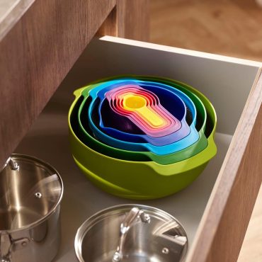 The Joseph Joseph Nest 9 set nested into one compact stack, sitting in an open kitchen drawer beside two stainless steel pots.