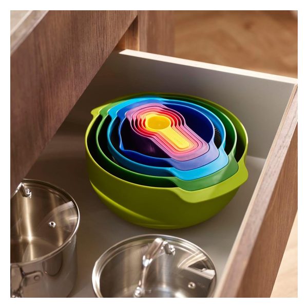 The Joseph Joseph Nest 9 set nested into one compact stack, sitting in an open kitchen drawer beside two stainless steel pots.