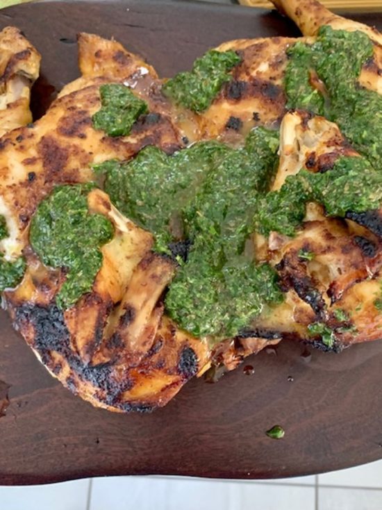 Golden split chicken topped with green herb salsa on a rustic wooden serving board.