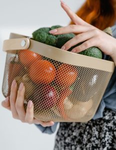 Person carrying a mesh basket of fresh tomatoes, broccoli, avocado and other vegetables