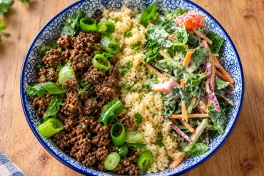 Blue-and-white bowl of spiced beef mince with spring onion, pale grainy rice substitute and creamy kaleslaw with tomato.