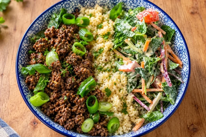 Blue-and-white bowl of spiced beef mince with spring onion, pale grainy rice substitute and creamy kaleslaw with tomato.