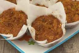 Golden-brown cheesy Italian muffins in white paper tulip cases on a blue-rimmed floral platter, with herbs and seeds on the baked tops.