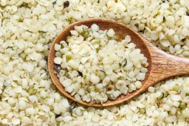 A wooden spoon holding hulled hemp seeds, resting in a bed of more hemp seeds.
