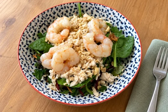 Vietnamese prawn and chicken salad with leafy greens in a blue-and-white patterned bowl on a wooden table.
